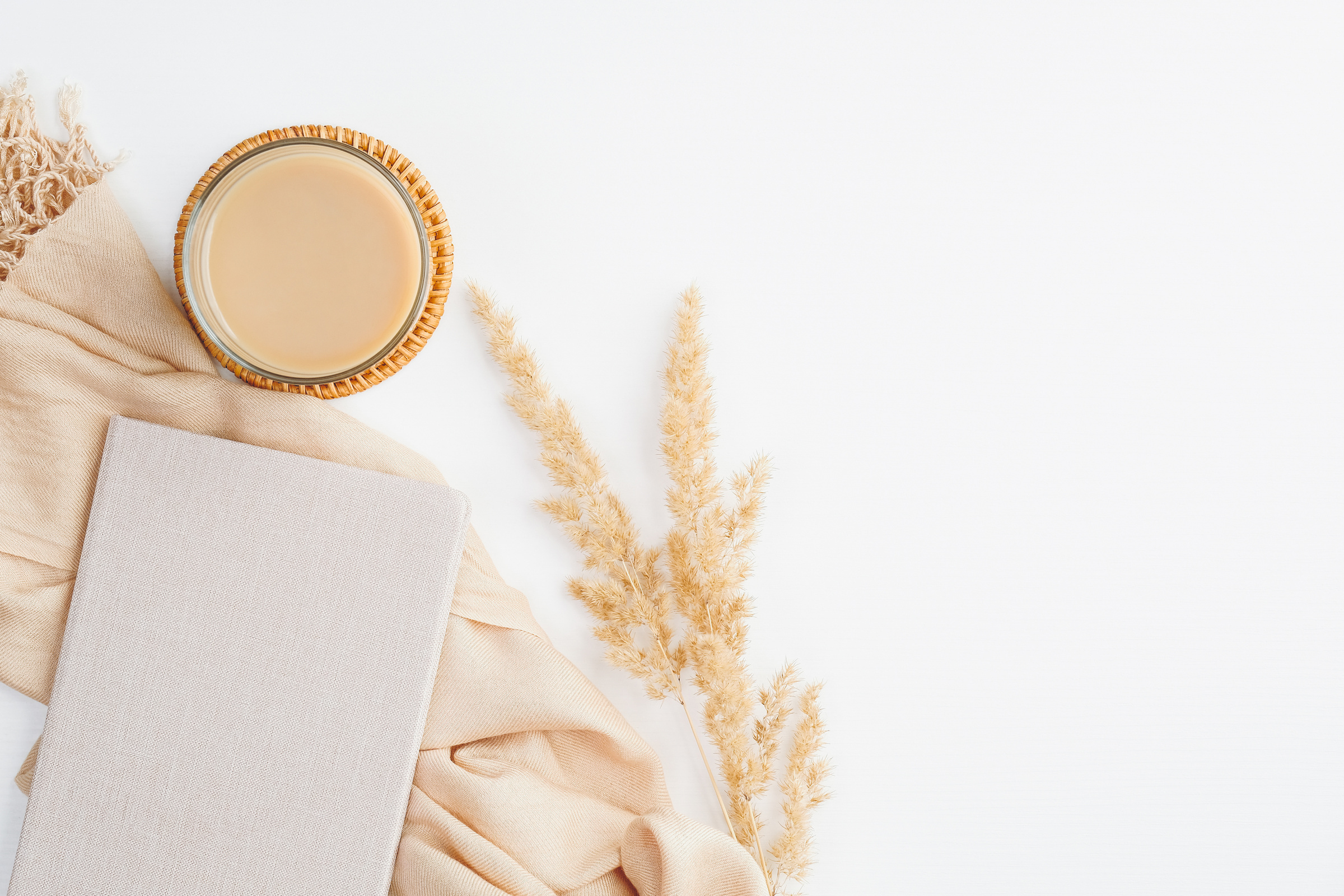 Flat lay, top view cozy home office desk. Beige blanket, cup of coffee, paper notebook and dry flowers on white table. Boho style feminine workspace.